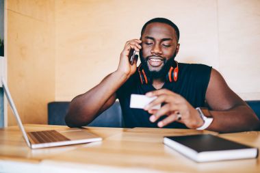 Pozitif afro Amerikan adam işleç ile ziyaret kartındaki bilgileri kontrol, kafede oturan bankacılık hakkında konuşma sırasında telefon danışmanlık sahip esmer erkek gülümseyen mil üzerinde bahsediyoruz
