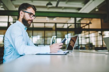 Durulması BT uzmanları için daha iyi görüş bildirim smartphone cep telefonu ile kontrol serin gözlük içinde sakallı. Yetenekli erkek programcı ofiste çalışmalar sırasında telefonla e-posta uygulaması yoluyla gönderme