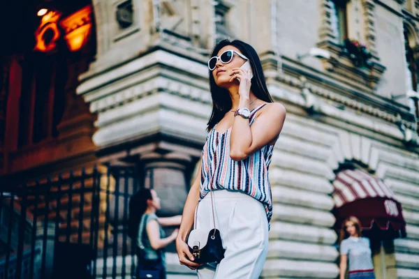 严重的女性在太阳镜和时髦的衣服上谈论在城市街道上的电话行走 有吸引力的年轻妇女有移动谈话使用连接在漫游漫步在空闲时间 — 图库照片