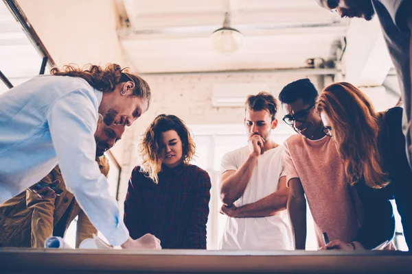 Concentrated group of architects drafting together having consultancy meeting in coworking space, skilled team of creative graphic designers making creative solution working on sketch for project