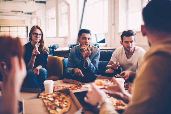 Multiracial group of international student talking to each other and making friends during pizza party, hungry male and female employees having lunch break together eating in coworking space
