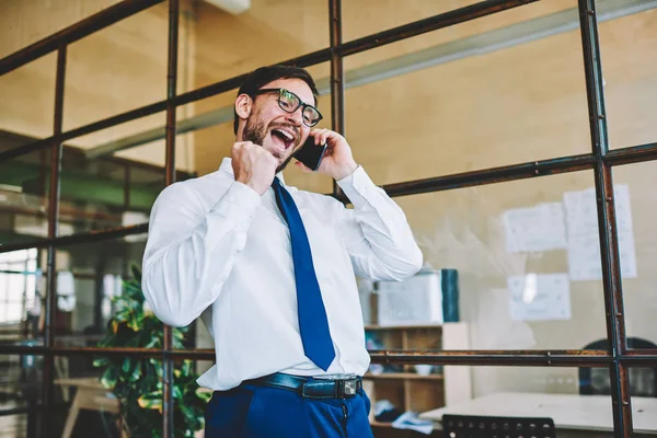 Amazed and excited entrepreneur with  winning Yes gesture celebrating successful news received by telephone conversation. Happy man office worker emotionally conversing via cellular feeling success