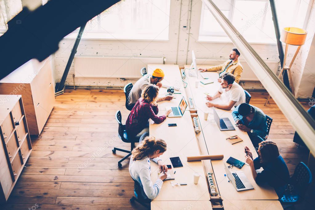 Top view of male and female members of crew sitting at desktop using technologies during working process,group of skilled developers concentrated on task cooperating and discussing ideas using laptops