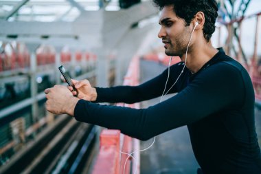 Sporcu yan görünüm etkin giymek egzersiz elinde tutan smartphone bağlı kulaklık dinleme müzik için giyinmiş. Adam telefonu spor eğitim için yükleme ses app Seçimi sığdır