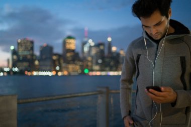 Giyinmiş genç adam spor eşofman açık havada akşam şehir arka plan ve smartphone aygıt yolu ile 4 g internet bağlantısı yükleme cool müzik ile ses çalar seçerek üzerinde duran