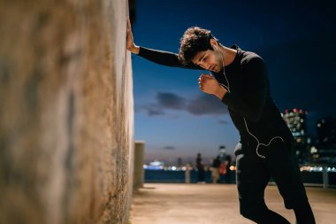 Delikanlı sevgilisi sporun kentsel ayarlarında çalıştığını akşam sonra duvara yaslanmış yorgun. Eşofman dinleme müzik kulaklık modern şehir içinde çalışmadan sonra mola sırasında yorgun erkek atlet
