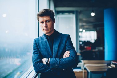 Ofis pencere, çapraz kolları kameraya bakarak zarif resmi takım elbise giymiş olan deneyimli iş adamı yakınındaki coworking ayakta müreffeh şirketinin emin erkek sahibi portresi yarım uzunluk