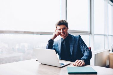 Formal giyim çatı iç ofis, başarılı erkek kurumsal Direktörü dizüstü bilgisayar başında oturan kamera bakarak iş için netbook kullanarak neşeli müreffeh busnessman portresi yarım uzunluk