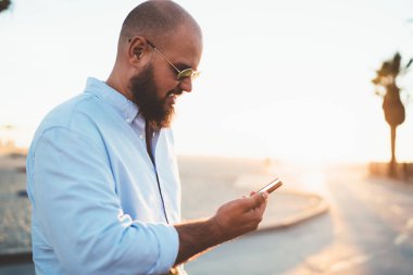 Hipster adam akıllı telefon app ağlardan online video izlerken güneş gözlüğü bağlantısı ile yakışıklı genç adam haber Gözat web sayfasında modern telefon güneşli hafta sonu dinlenme okuma memnun.