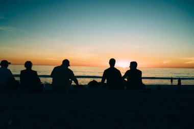 Genç arkadaşlar birlikte recreationg alacakaranlıkta zevk tatil yaz, güzel gün batımı ve altın manzarası sakin okyanus su surfac bakarak halklar siluet akşam içinde kum plajındaki