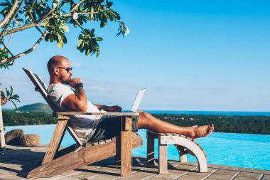 Sakallı işadamı mavi havuzu boş kopya alanı ekran reklam içeriğini uzaktan yaz resort tropikal yöredeki sırasında çalışma için netbook klavye üzerinde metin yazarken yalan