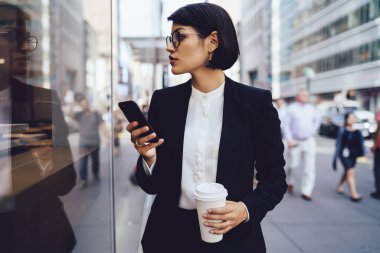 Megalopolis elinde lezzetli kahve ile sokakta yürürken Eyewear ciddi kadın tüccarı. Şık resmi emin işkadını giymek uzakta tutarak cep telefonu ve kahve arıyor
