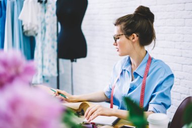 Şık gözlük ve masaüstü ve çizim kroki için Tekstil giyim koleksiyonu oturan moda atelier çalışma terzi ölçme bant dalgın yetenekli genç kadın. Kopyalama alanı alanı