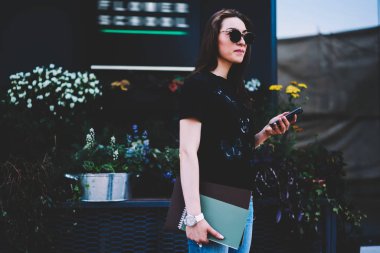 Smartphone cep telefonu ile Internet bağlantısı paylaşımı için ağa genç çekici kız öğrenci dosya yükleme serin güneş gözlüğü. Sokağı'nda yürüyüş ve modern teknoloji kullanarak güzel hippi kız