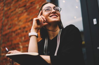 Gülümseyen güzel genç uzağa bakarak ve uygulanması için başarılı fikirler düşünmeye trendy Eyewear closeup görüntüsü. Büyüleyici olumlu hippi kız zevk eğlence anda kentsel ayarı