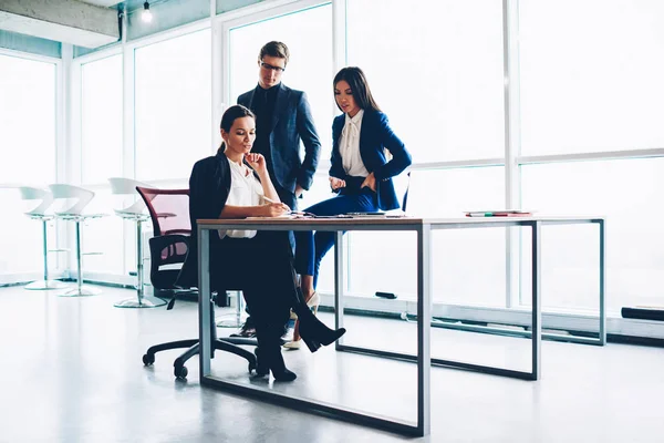 Confident female owner or corporation checking financial report and accountings during meeting with employees. proud ceo writing business plan controlling working process in company sitting at desktop