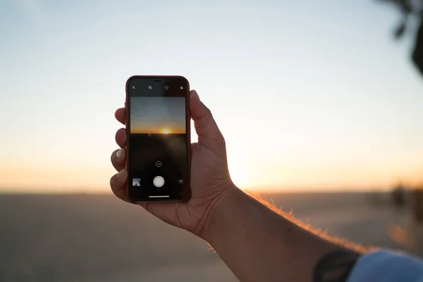 電話のカメラで夕日とスカイラインのビデオ撮影の男性のクローズ アップ表示を美しい日没の夕方の写真を撮るためのアプリケーションを使用して近代的なスマート フォンを保持している人間の手の画像をトリミングするには — ストック写真