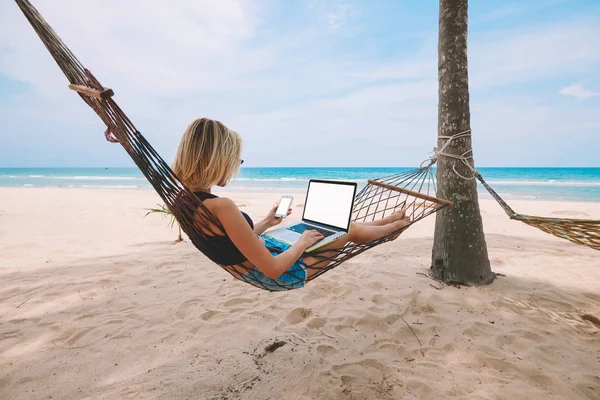 女自由职业者的企业家躺在吊床上 做远程商务工作在现代笔记本电脑与空白屏幕区域的智能手机网页在热带海滨夏季假期 — 图库照片