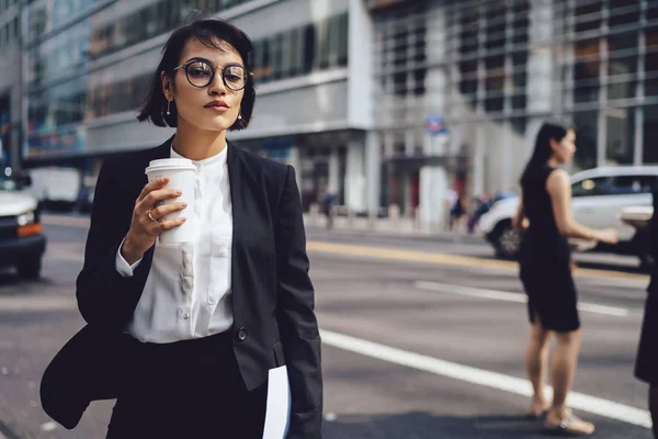 Confident businesswoman in formal wear hurrying walking to office near publicity area for business information.Female manager in stylish spectacles strolling in New York town while coffee to go outdoor