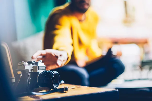形象模糊的男性摄影师身着黄色毛衣 拿着老式相机与现代镜头在手 精选的焦点在时尚古董设备做相片在桌上 — 图库照片