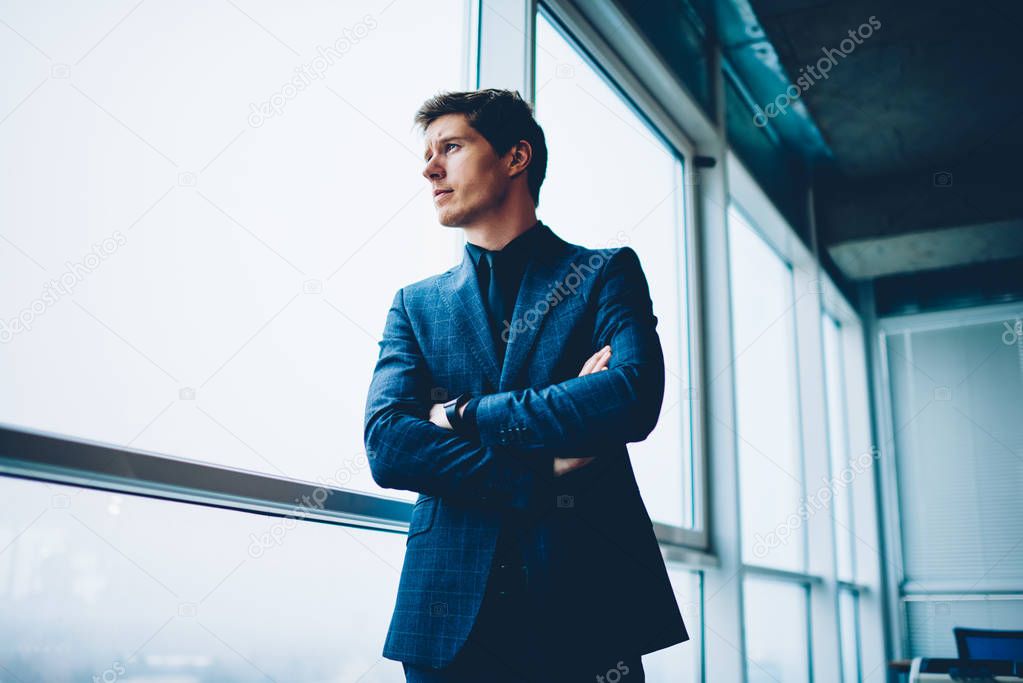 Pensive prosperous businessman in formal outfit looking away in window thinking about future plans and projects,handsome male executive manager puzzled on creative solution for corporation in office