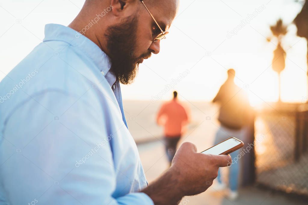 Selective focus, hipster guy checking mail on smartphone sending message via good internet connection on street, young handsome man chatting in social networks using application on telephone outdoors