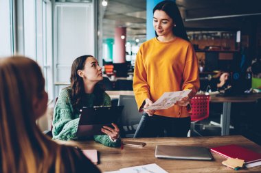 Ofis iç beyin fırtınası sırasında genç kadınlar yeni tasarımı hakkında konuşmak kroki. Yetenekli öğrenciler vasıl okul sırası şık Studio oturan moda giysiler planı birlikte çalışma