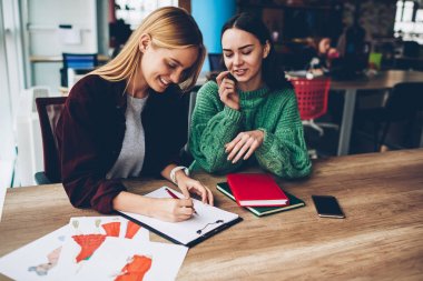 Ahşap masaüstünde çalışan yeni moda proje için kroki çizim neşeli iki yaratıcı tasarımcılar. Pozitif öğrenciler üniversitede oturan görev üzerinde birlikte. Başarılı kadın teamworking ofiste