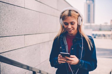 Müzik Playlist telefon indirmek için internet sitesinde seçme denim giyim gülümseyen genç kadın. Online sohbet ederken cep için olumlu öğrenci dinleme şarkıları kulaklık bağlı