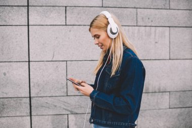 Hippi kız kot giyim gri promosyon arka plan yürüyüş modern Kulaklığımda dinlemek için smartphone cep telefonu ile müzik uygulamasında ses şarkı seçme giymiş yan görünüm