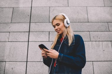 Modern Kulaklığımda çalma listesinden serin müzik dinleme sırasında e-posta kontrol denim ceket gülümseyen hippi kız Smartphone-e doğru bağlı. Neşeli erkek sesli telefon açık havada yürüyüş üzerinde kitap İndiriyor