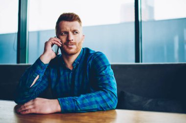 Uzay coworking istirahat smartphone aygıt üzerinde arkadaşlarınızla konuşurken Kızıl saçlı yakışıklı genç adam. Casual gömlek cep telefonu kafede oturan iletişim hipster adam giymiş