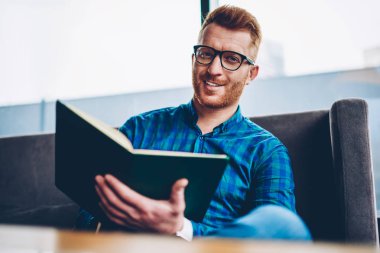 Kızıl saçlı mali belgeler gözlük kendi kahve shop.ositive öğrencinin elinde kitapla oturan denetlerken kameraya gülümseyen neşeli yakışıklı erkek girişimci portresi