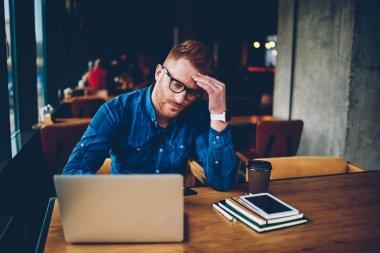 E-öğrenme dizüstü bilgisayar, gelen yorgun kırmızı saçlı yetenekli öğrenci gözlük içinde tükenmiş. İzlerken sıkıcı webinar modern netbook, ahşap masa kafede kahve ile oturmak, genç adam