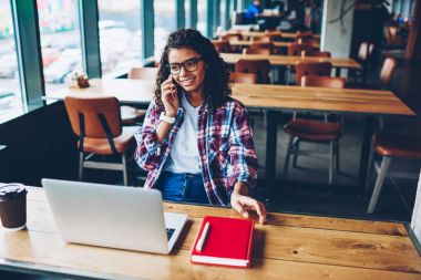 Dizüstü bilgisayar eğitim için Kablosuz 4 g bağlıyken smartphone aygıt üzerinde dostu mobil konuşma sırasında gülüyor olumlu Afro-Amerikan öğrenci üniversitede oturan internet