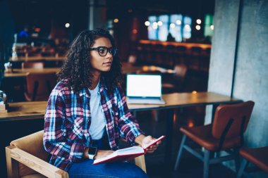 Zeki Afro-Amerikan öğrenci kıvırcık saçlı edebiyat kitap kütüphane kullanarak seminer için hazırlanıyor. Boş ekran alanı ile modern netbook. Koyu tenli teen uzakta arıyorum elinde ders kitabı ile
