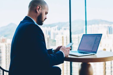 Ofis iç metin reklam için lapto bilgisayar wth sahte alanı oturan smartphone aygıt üzerinde önemli bilgileri içeren bildirim gönderme şık elbiseli dalgın sakallı yönetmen