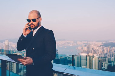 Şık güneş gözlüğü ve zarif elbise tarafından medya dijital Touch güncelleştirilirken bakarım emin işadamı yan görünüm yastık balkon teras üzerinde duran zevk metropolis görünümü