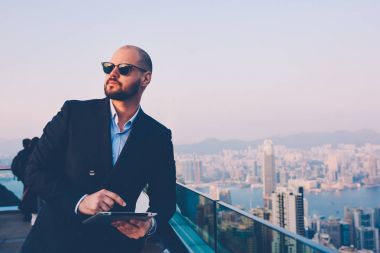 Şık güneş gözlüğü ve zarif elbise tarafından medya dijital Touch güncelleştirilirken bakarım emin işadamı yan görünüm yastık balkon teras üzerinde duran zevk metropolis görünümü