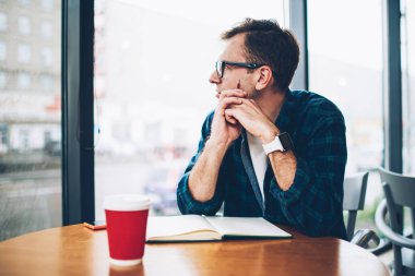 Genç yaratıcı erkek blogger penceresine bakarak ve kişisel web sitesi için iyi yayın hakkında durulması trendy kıyafetler giymiş. Kapalı sınavlarına hazırlanıyor gözlük dalgın zeki öğrenci