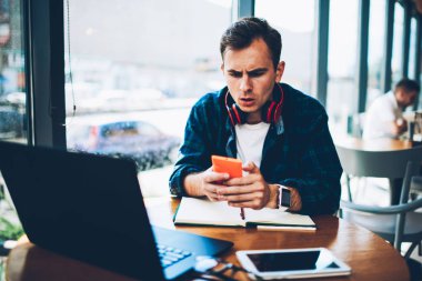 Genç iyi hipster adam smartphone kablosuz internet'e bağlı alınan cep telefonu operatörü bildirim tarafından sürpriz arıyor. Duygusal erkek kişi mesaj e-posta mesajı kafede modern telefon