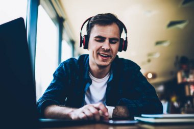 İyi gülümseyen erkek öğrenci arıyorsunuz komik müzik ve yeni kompozisyonlar smartphone cep telefonu ile arama için 4 g bağlı. Genç olumlu zevk kafede oturan kulaklıklar ve aygıt ile adam