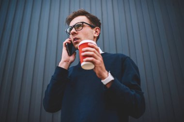 Yakışıklı hipster adam smartphone uygulama ve Internet kullanarak mobil konuşmayı gündelik kıyafeti giymiş. Ayarlama ve telefonda konuşurken take away kahve ile Caddesi'nde yürüyen genç adam