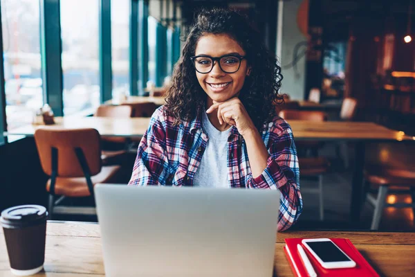 成功的非洲裔美国学生的肖像与卷曲的头发和眼镜微笑着在笔记本电脑与互联网连接在大学的搜索信息坐在膝上型计算机上 — 图库照片