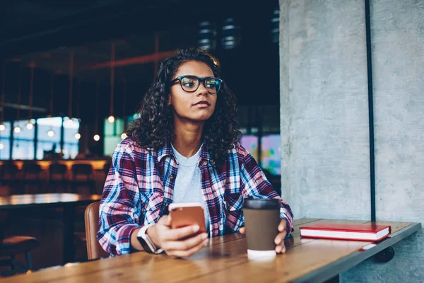 Afro-Amerikan hipster kız arkadaşına smartphone cep telefonu ile sms mesaj yollama mola sırasında git kahve ile dinlenme Eyewear. Koyu tenli teen el kitabı ile masaüstünde oturan telefon ile