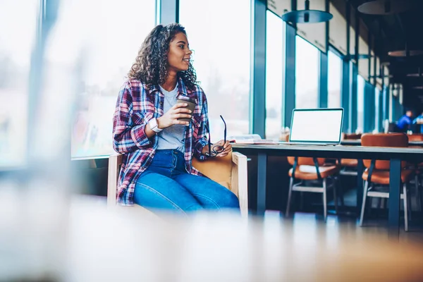 Rekreasyon vaktinizi üniversitede bir kahve molası sırasında kıvırcık saçlı sevimli Afrikalı-Amerikalı genç kadın. Koyu tenli öğrenci Kitaplığı'nda lezzetli içecek ile dinlenme rahat gömlek giymiş