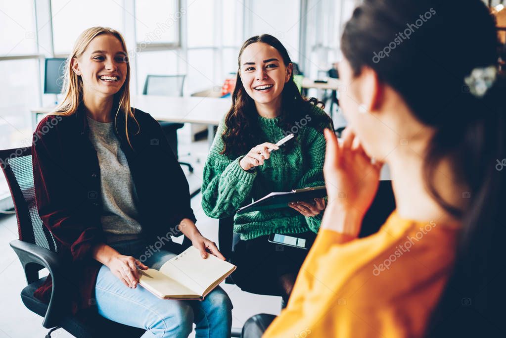 Cheerful female designers laughing during morning briefing in office interior.Positive colleagues discussing productive strategy for developing own businee startup project during friendly meeting