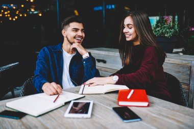 Neşeyle dostça konuşma yaparken gülümseyen mutlu kadın ve erkek öğrenciler, Teras kafe üzerinde oturan ortak projeler üzerinde çalışma neşeli arkadaşlarım şaka ve tartışma sırasında gülüyor