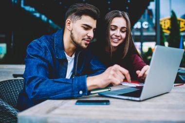 Mutlu erkek ve kadın en iyi arkadaşlar eğlenmeye Cafe teras ile laptop, neşeli genç öğrenciler web sayfasında online bilet rezervasyonu sırasında bilgi arama dinlenme komik video izlemek