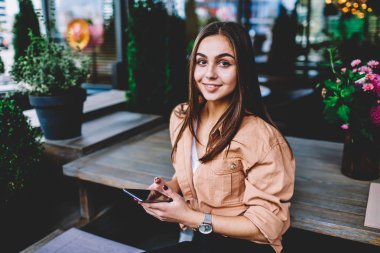 Genç ve güzel hippi kız rahat kıyafet üstünde hareket eden telefon popüler uygulamasını kullanırken kameraya bakarak akıllı telefon, Cafe iç gönderen mesajla dinlenme şirin kız öğrencinin portresi